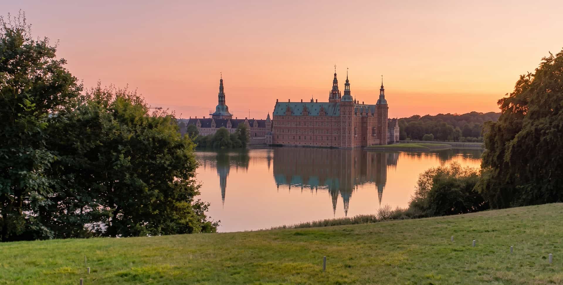 Frederiksborg Slot belyst af gylden solnedgang med vandspejling i Slotssøen ved Hypnohuset Hillerød